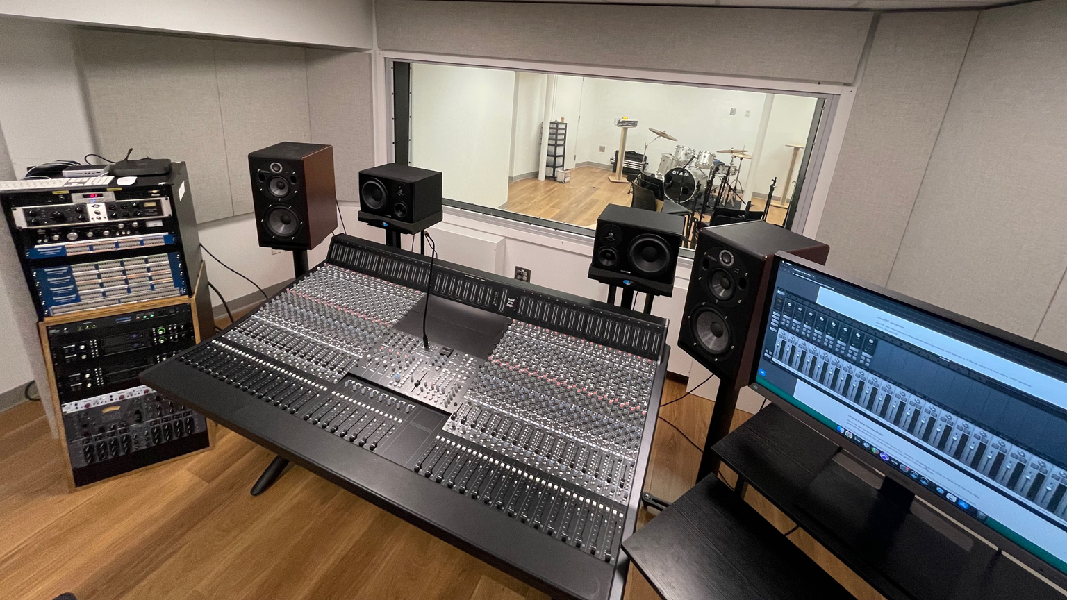Control room in the recording studio showing equipment racks, monitors, mixing board, and display