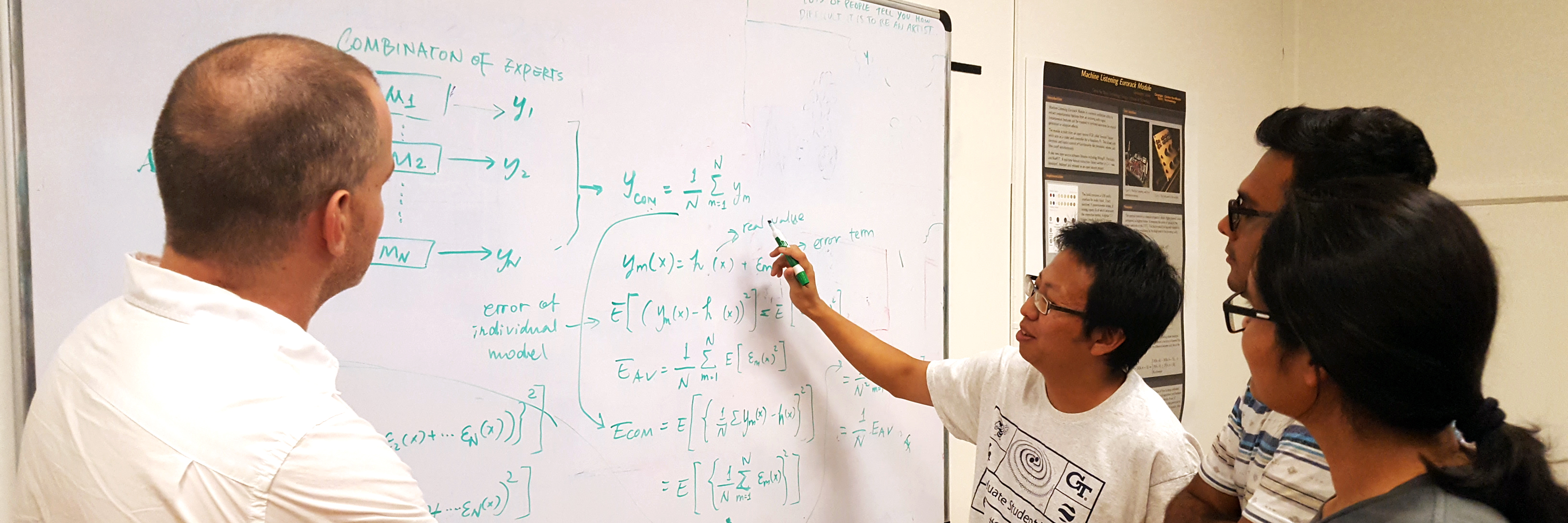 Three students discuss a class topic with a professor, pointing to a white board.