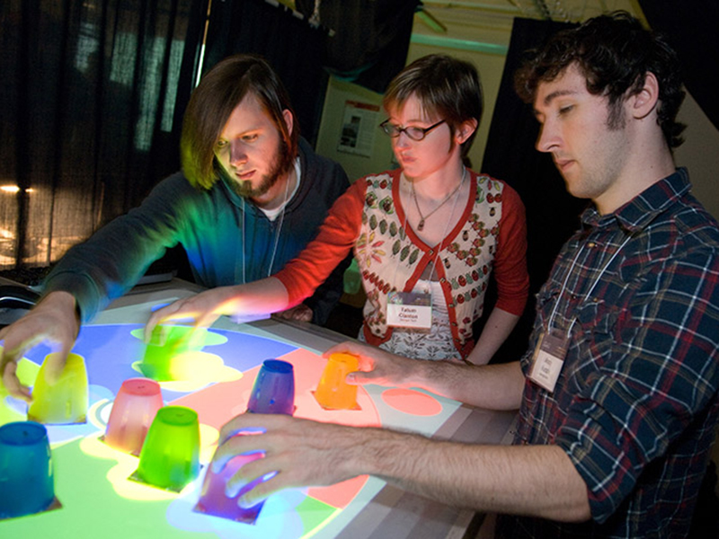 Three students performing an experiment with colored cups on a table with corresponding colors and sensors.
