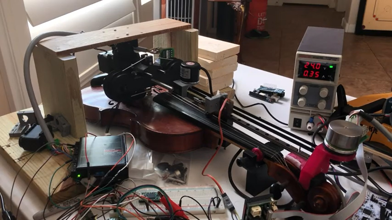 A violin attached to a robot that is controlling it and playing it.