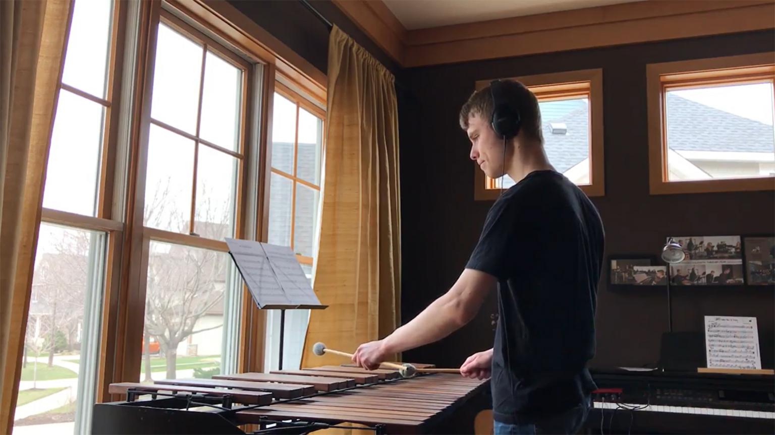A student playing a set of marimbas in front of a window.
