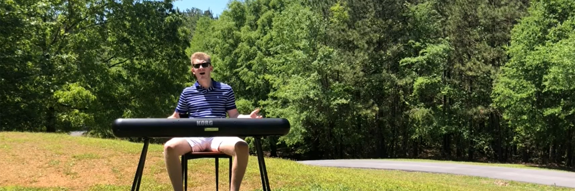 A student playing a keyboard outside on a hill by a country road.