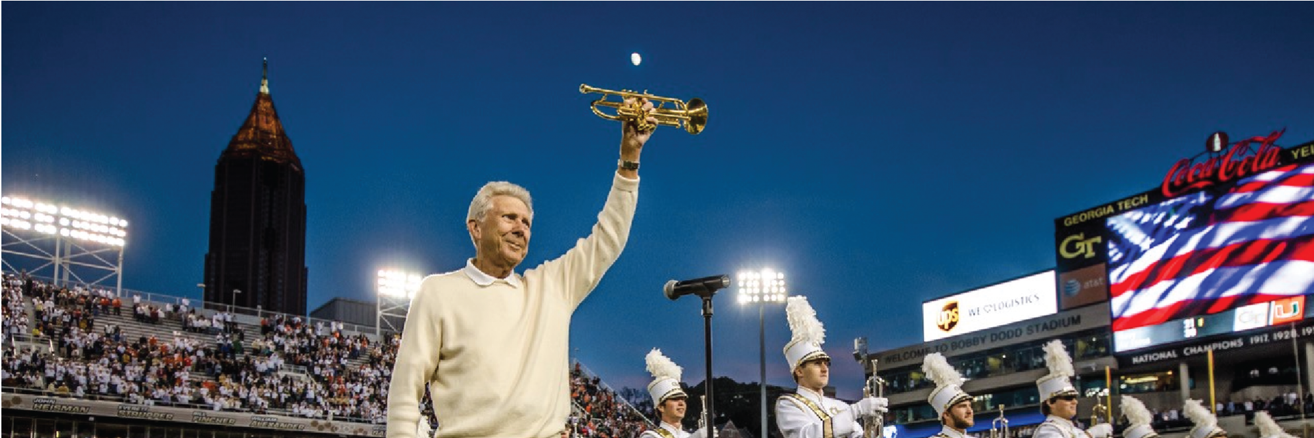 Cecil Welch holds his trumpet above his head in front of the marching band