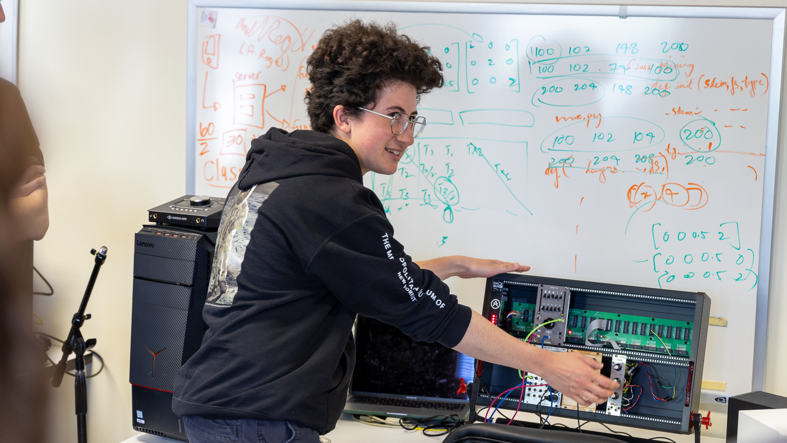 Mir Jeffres pointing to a synthesizer in front of whiteboard showing matrix math