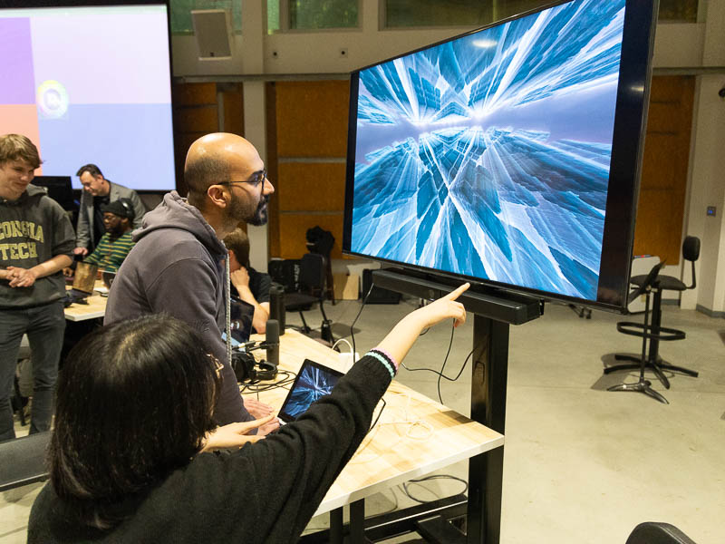 Students point to a monitor showing an abstract display of lines