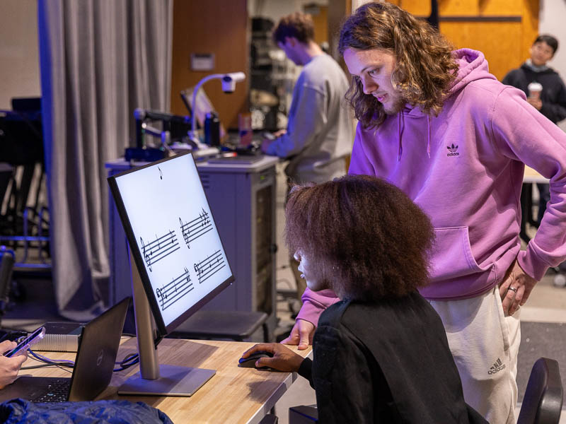 Student playing a game involving music notation as another looks on