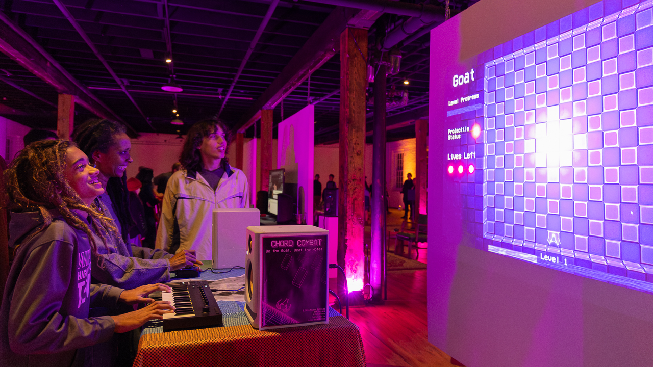 People playing Chord Combat, a video game controlled by playing chords on a small piano keyboard.